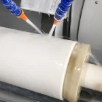 A large ceramic cylinder is being wet ground with coolant during the ceramic finishing and machining process.